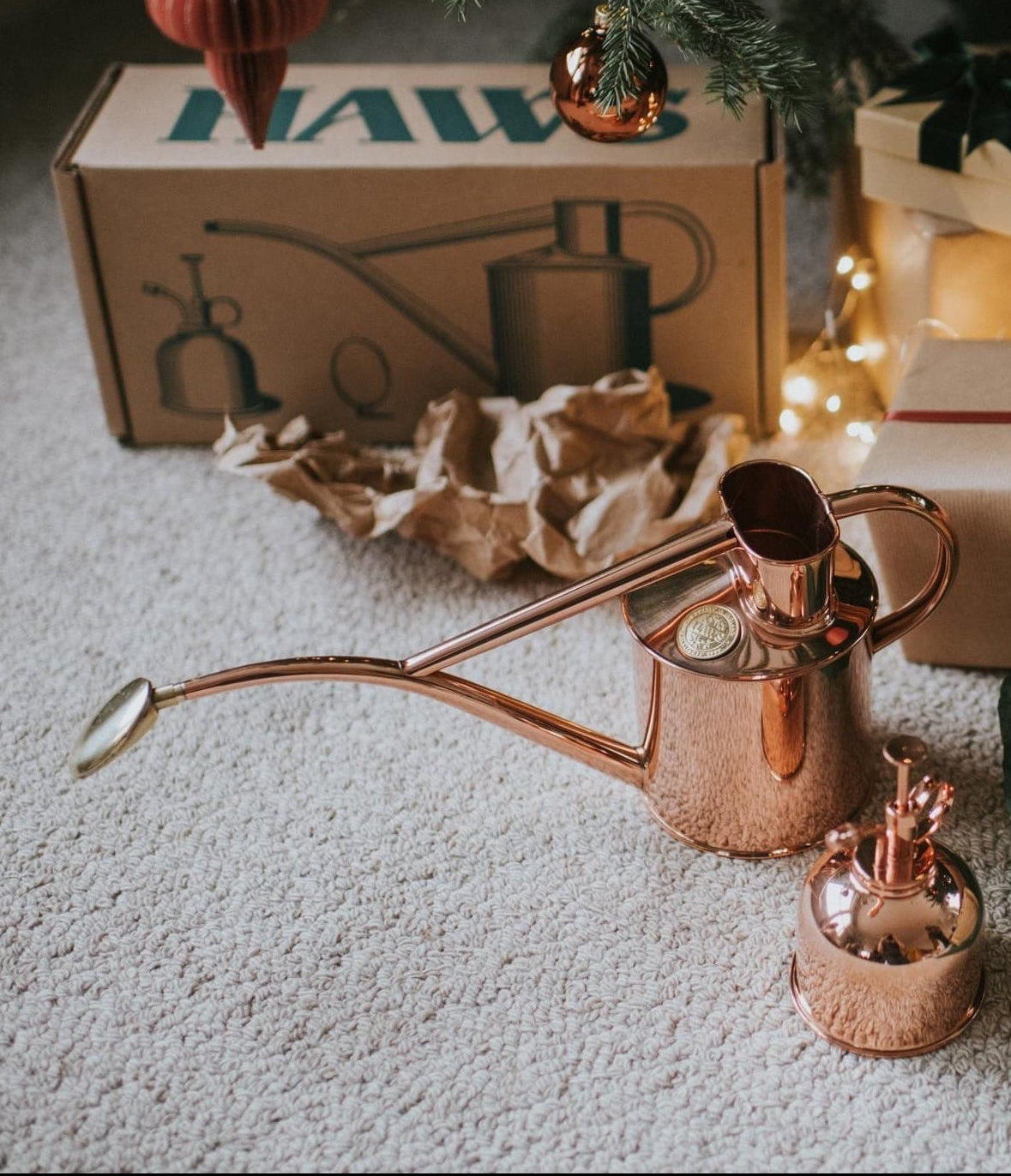Copper watering can on a carpeted floor with Christmas presents and decorations.