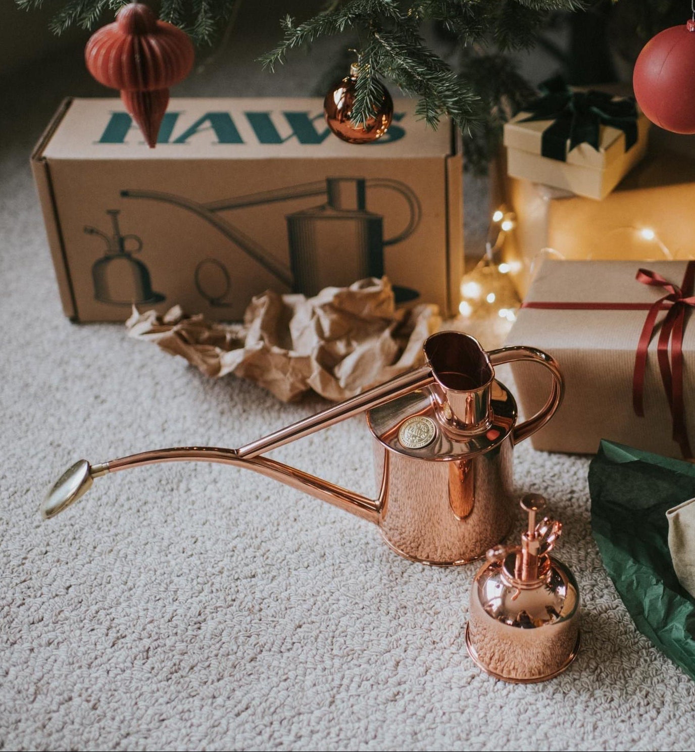 Copper watering can on a carpeted floor with Christmas presents and decorations.